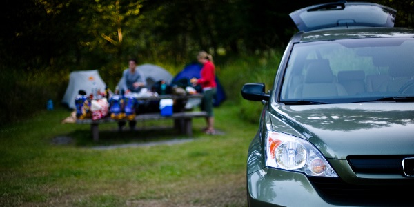 Estate car with tailgate open, family with camping equipment in background